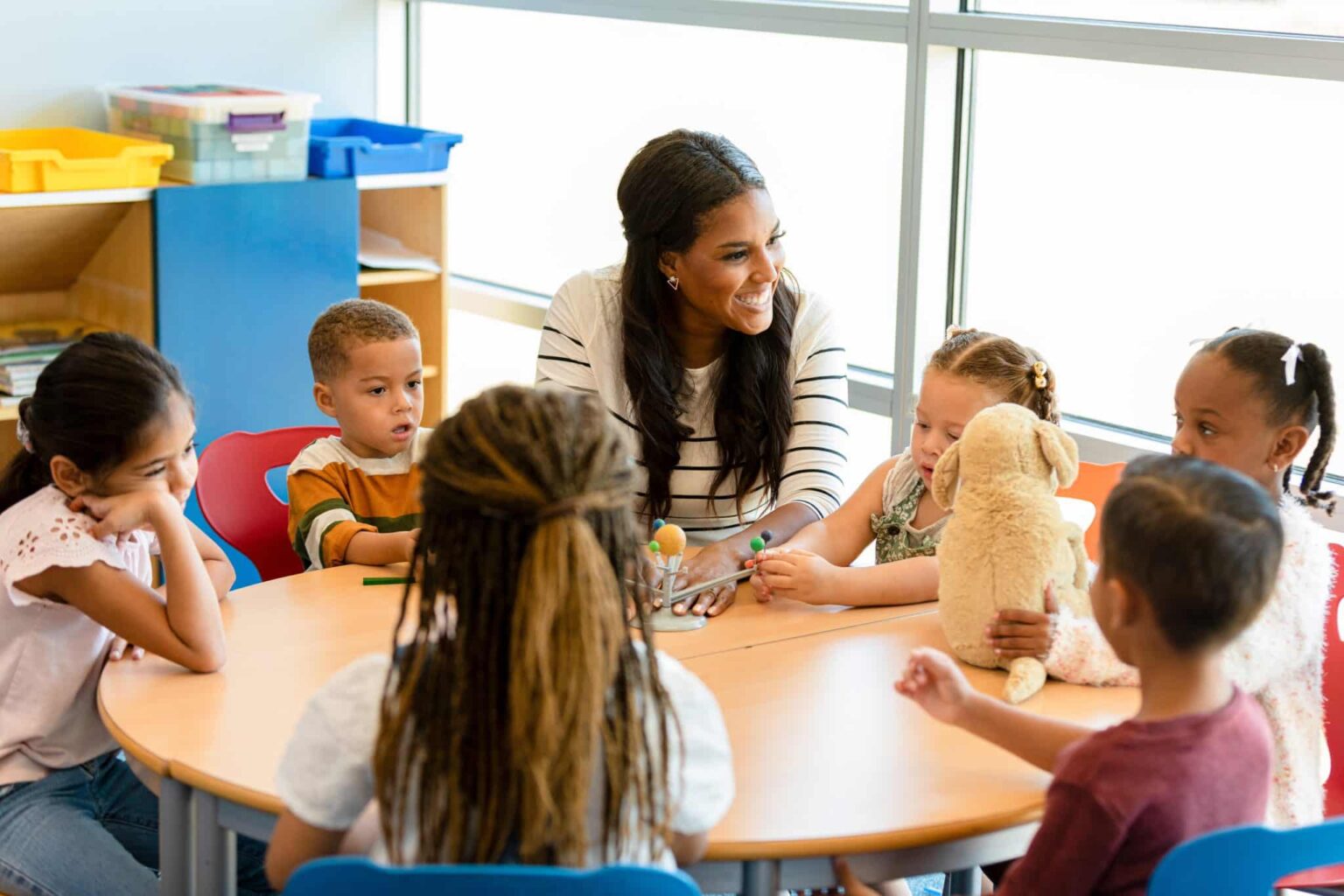 Teacher of small children at a table showing 6 seated children a small model of the solar system.